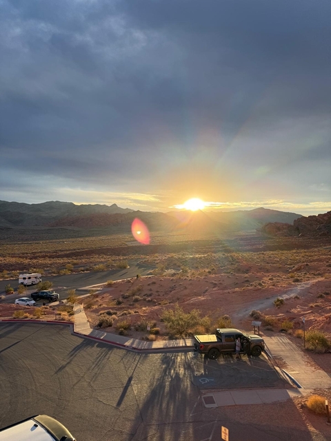 Sunset over a desert landscape with parked cars.