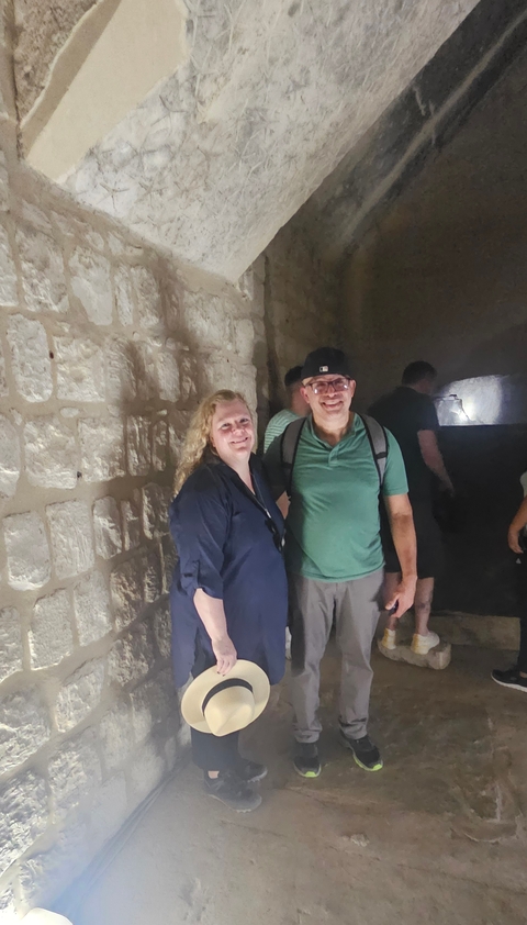       A couple standing inside a dimly lit stone structure.
  