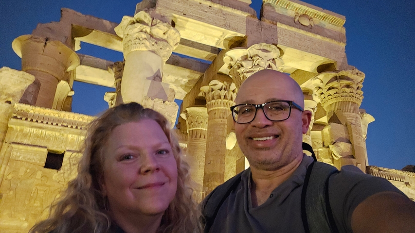 A couple posing in front of illuminated ancient ruins at night.