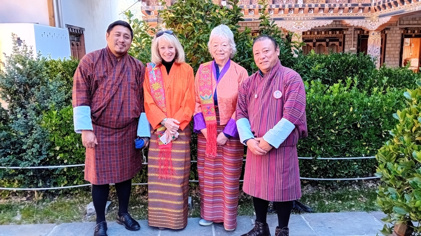       Four people in colorful traditional Bhutanese clothing posing outdoors.
  