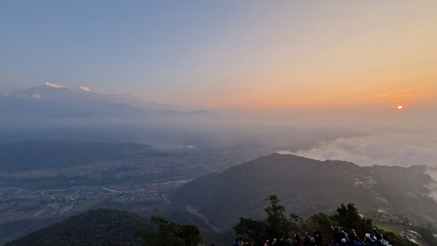       A panoramic view of a mountainous region with the sun setting.
  