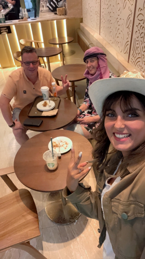       A person smiling and enjoying a meal with friends in a casual dining setting.
  