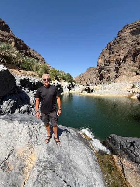 Man standing next to a water canyon in a rocky desert.