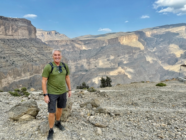 Person posing on rocky terrain with dramatic cliffs in the background.