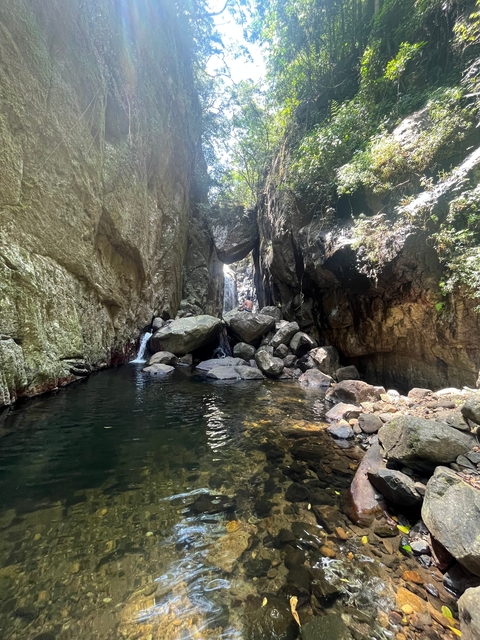       Person sitting on rocks at the edge of a water pool in a canyon.
  