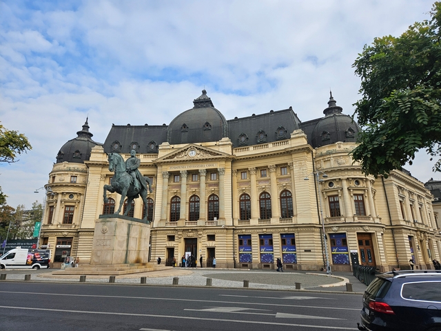A historic building with a statue in front, with people around.
