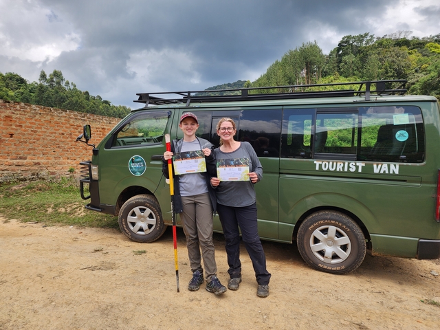       Two people holding certificates in front of a tourist van.
  