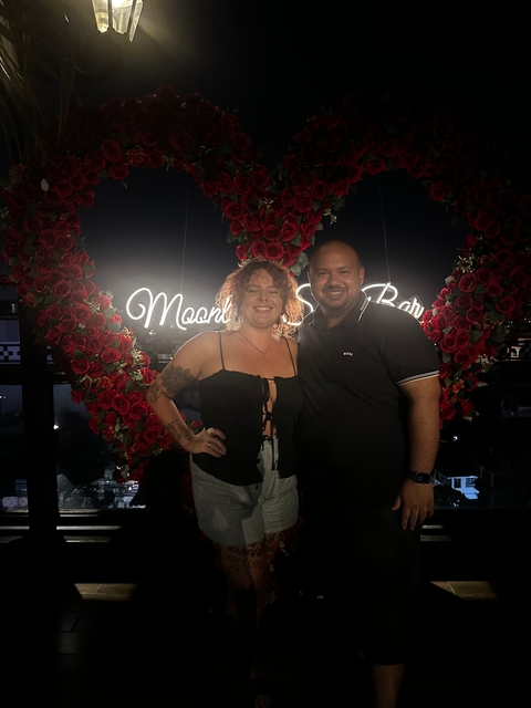 Two people posing in front of illuminated signage with roses at night.