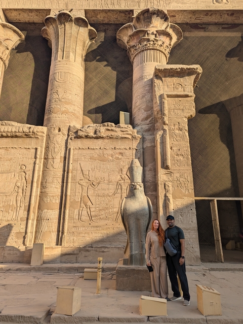Tourists posing by large ancient carvings on a temple.