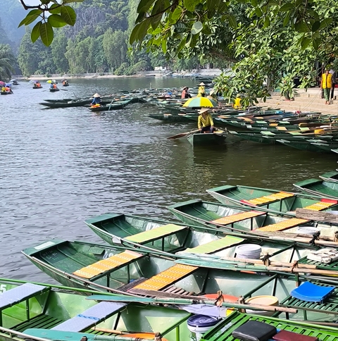       Rowboats parked along a river with people.
  
