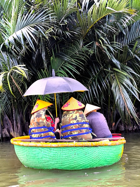       People sitting in a boat under palm trees with umbrellas.
  