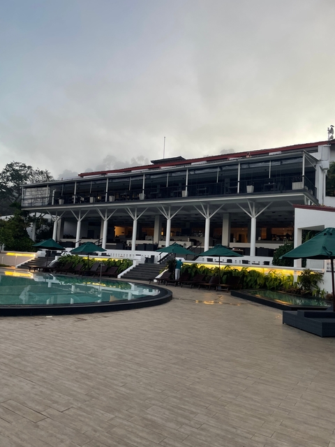       Modern hotel building with a swimming pool and sunbeds.
  