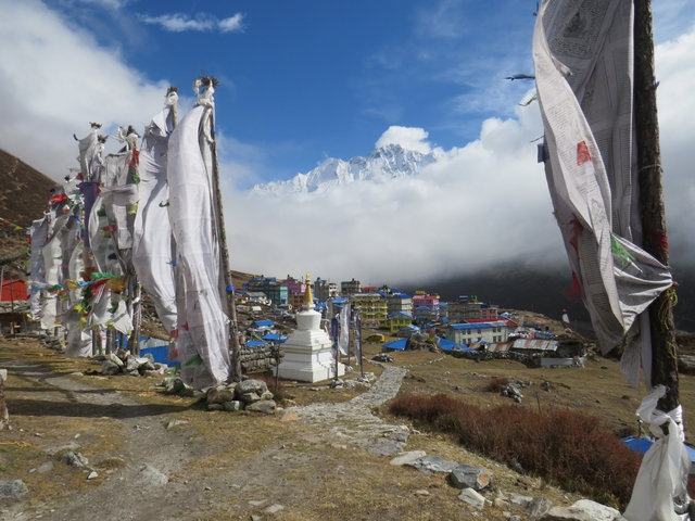 Prayer flags and a mountain village overlooking a snow-capped peak.