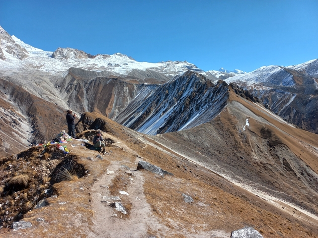 People sitting on a ridge with snow-capped mountains in the background.