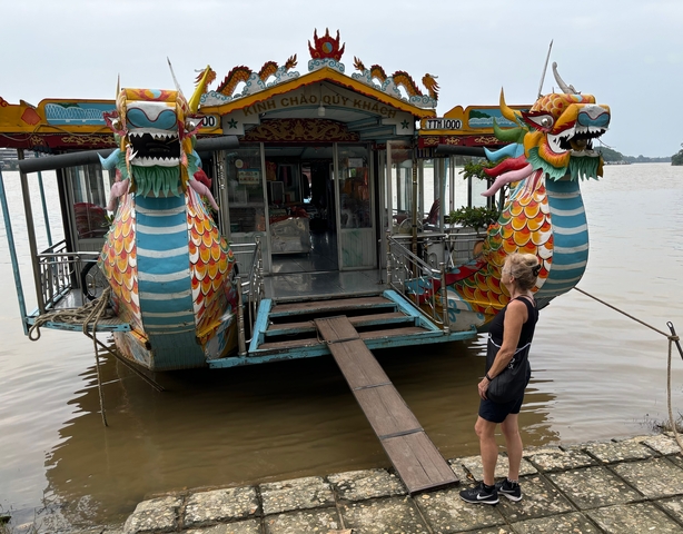 Colorful tour boat with dragon motifs docked by a river.