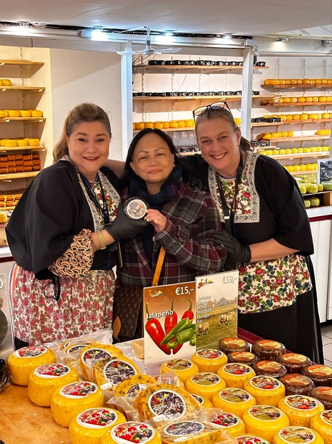 Three women in traditional attire smiling at a market stall.