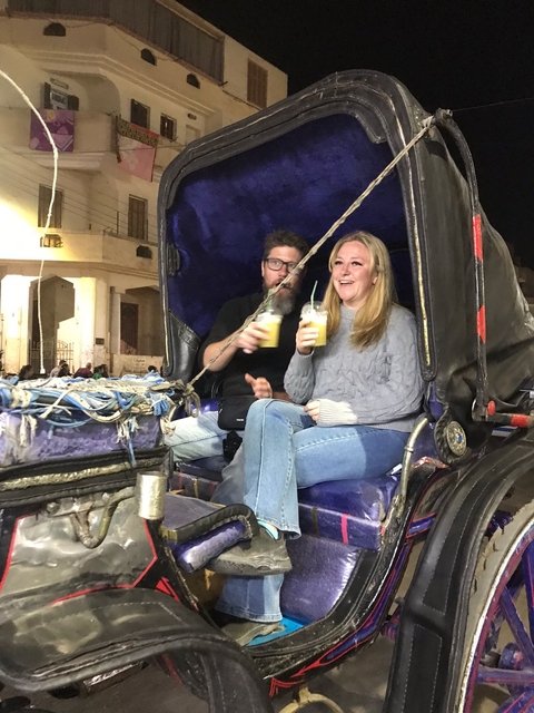 A couple enjoying drinks inside a horse-drawn carriage at night.