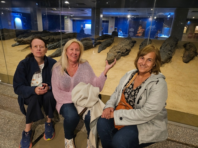       Three women posing inside a museum beside historical artifacts.
  