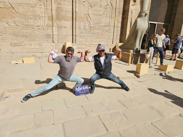       Two people posing with a tourist sign in front of an ancient temple.
  