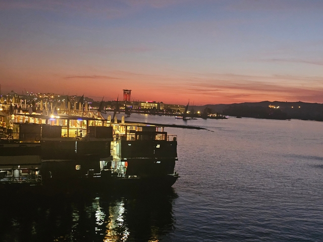 Cityscape and river at sunset with boats docked.