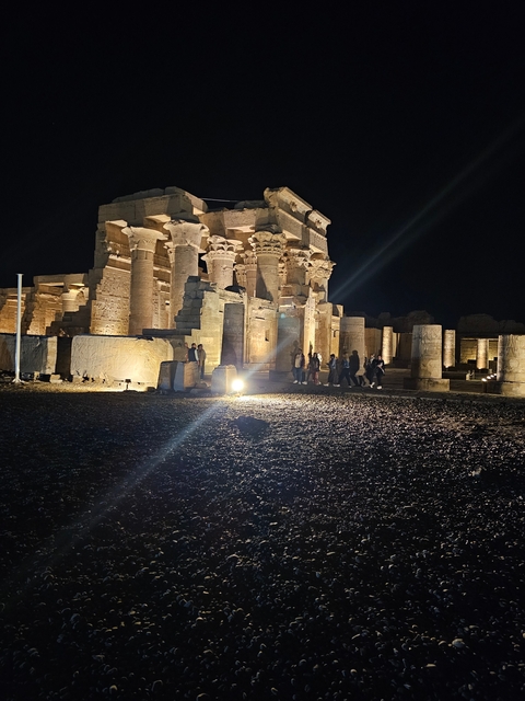 Ancient temple with columns and people visiting, illuminated at night.