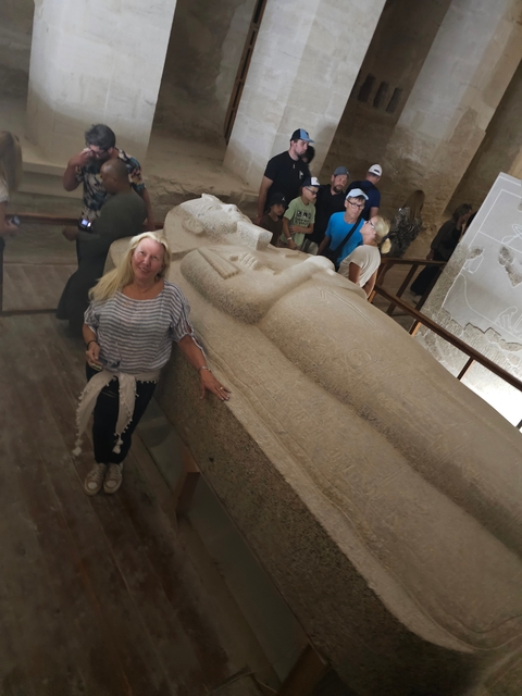       Woman posing beside a large ancient sarcophagus indoors.
  