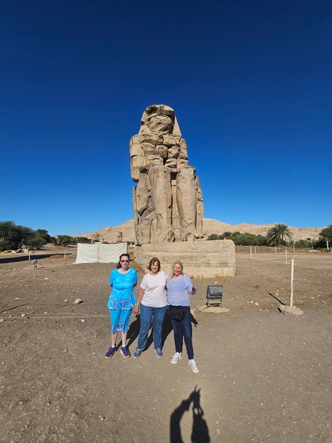 Three people standing in front of an ancient colossal statue.