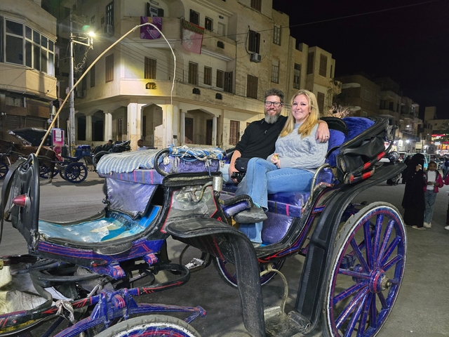 Couple seated in a horse-drawn carriage at night.