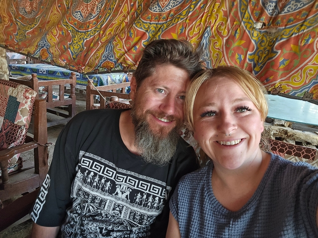 Two people smiling inside a colorful, patterned tent.
