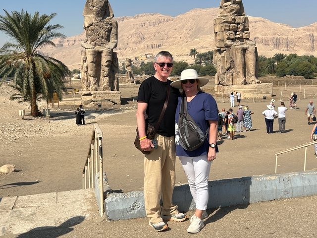 Tourists standing near ancient statues in barren landscape.