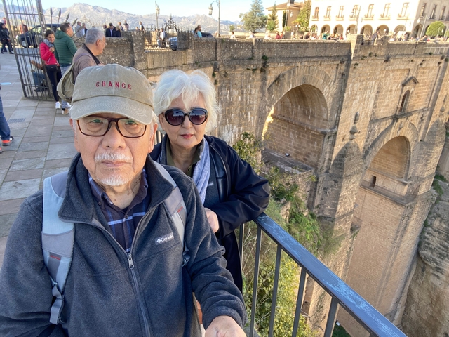 Elderly couple in front of a large stone bridge.