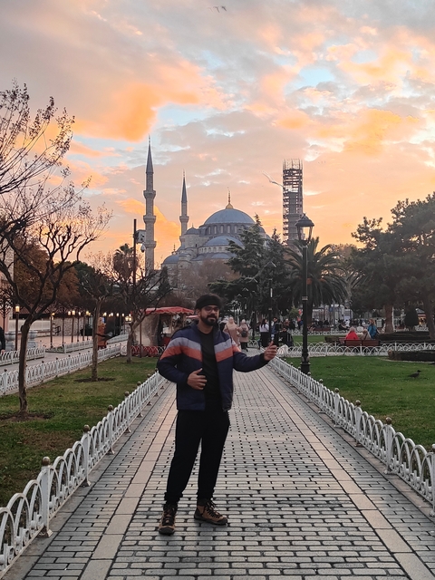 A man posing in front of a mosque during sunset.