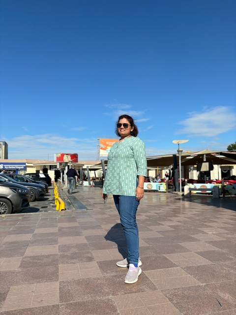 Person standing in a plaza with shops and cafes in the background.