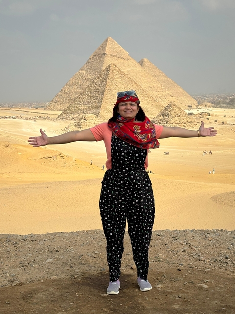 Person posing with arms outstretched in front of pyramids.