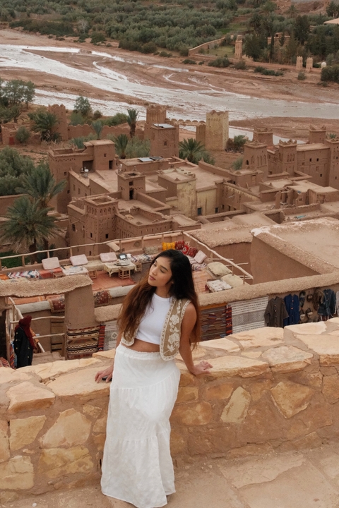       Person posing in front of traditional mudbrick structures.
  