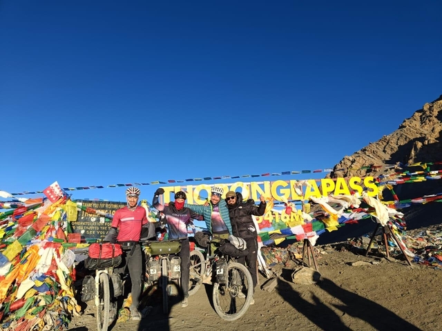 Cyclists posing at the summit of a mountain pass with flags and sign.