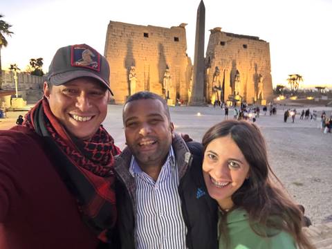 Three people posing in front of temple ruins at sunset.