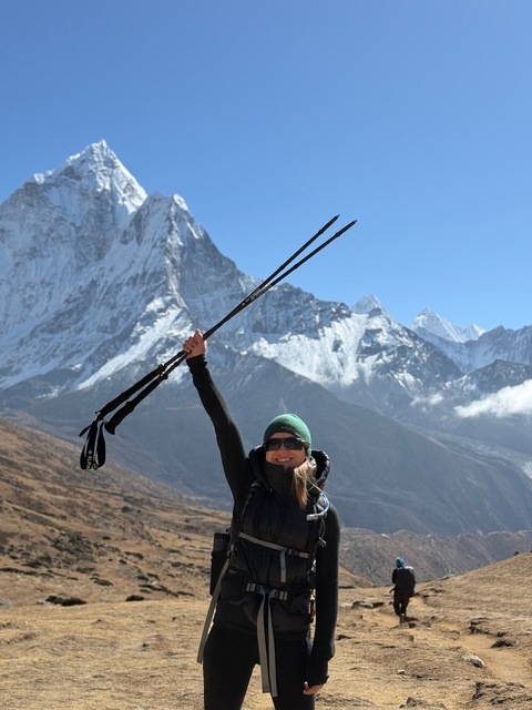 Woman celebrating with trekking poles in front of snowy mountains.