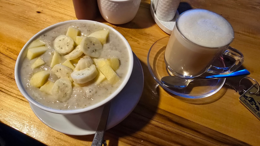       Bowl of oatmeal with bananas and apples next to a cappuccino.
  