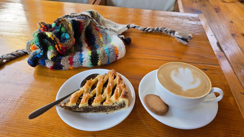       A knitted hat next to a cappuccino and pastry on a wooden table.
  