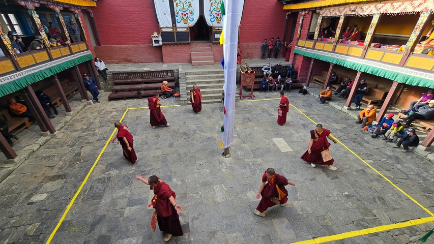       Monks rehearsing a dance in a temple courtyard with spectators.
  