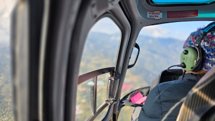 View from inside a helicopter showing a pilot and mountainous view.