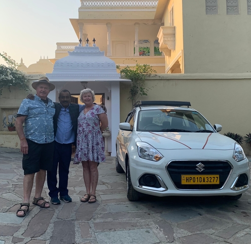 Three people standing next to a car in a courtyard.