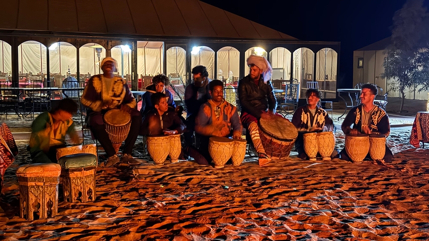 Group of people playing drums at night in a desert camp.