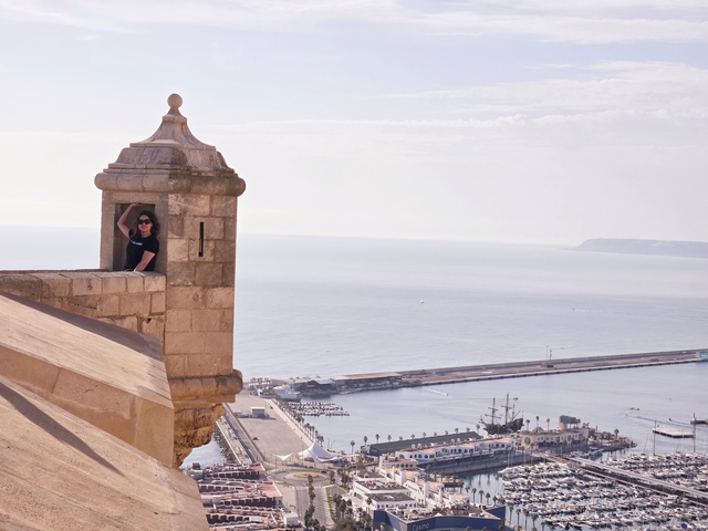       A person posing at a coastal fortress with panoramic sea views.
  