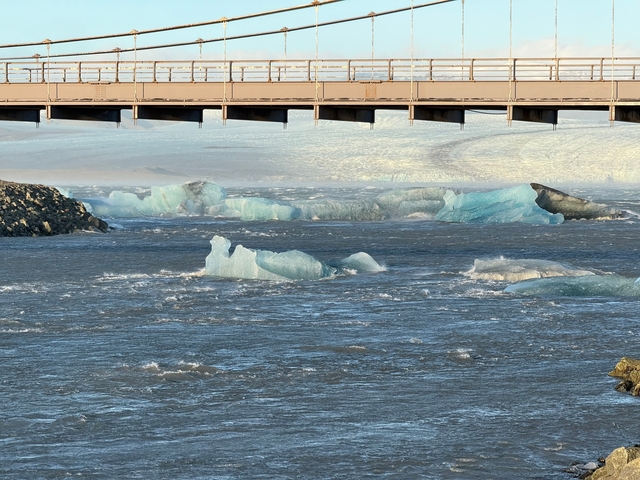       Large chunks of ice floating in a river under a bridge.
  