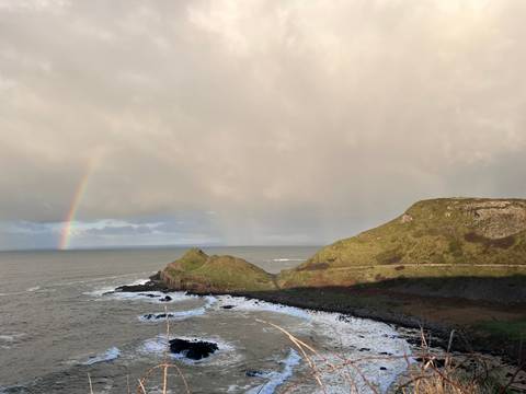 A rainbow over a coastal landscape surrounded by cliffs.