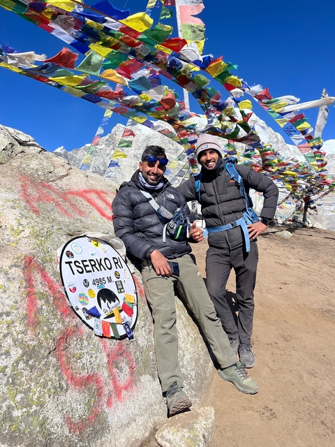 Two hikers standing beside a cairn with prayer flags.