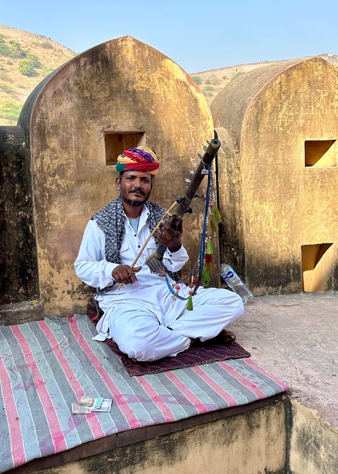       Man in traditional attire playing a musical instrument.
  