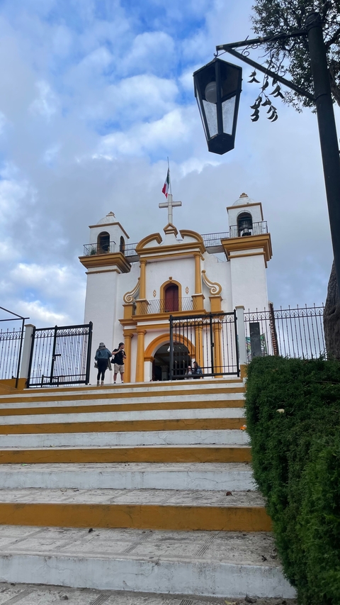       Visitors walking in front of a white church with orange trim.
  